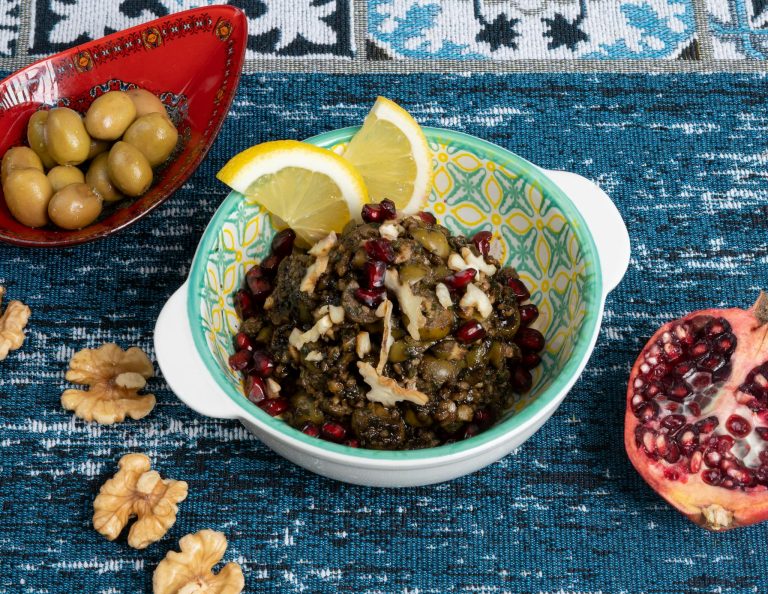 A bowl of food with olives, pomegranate and nuts