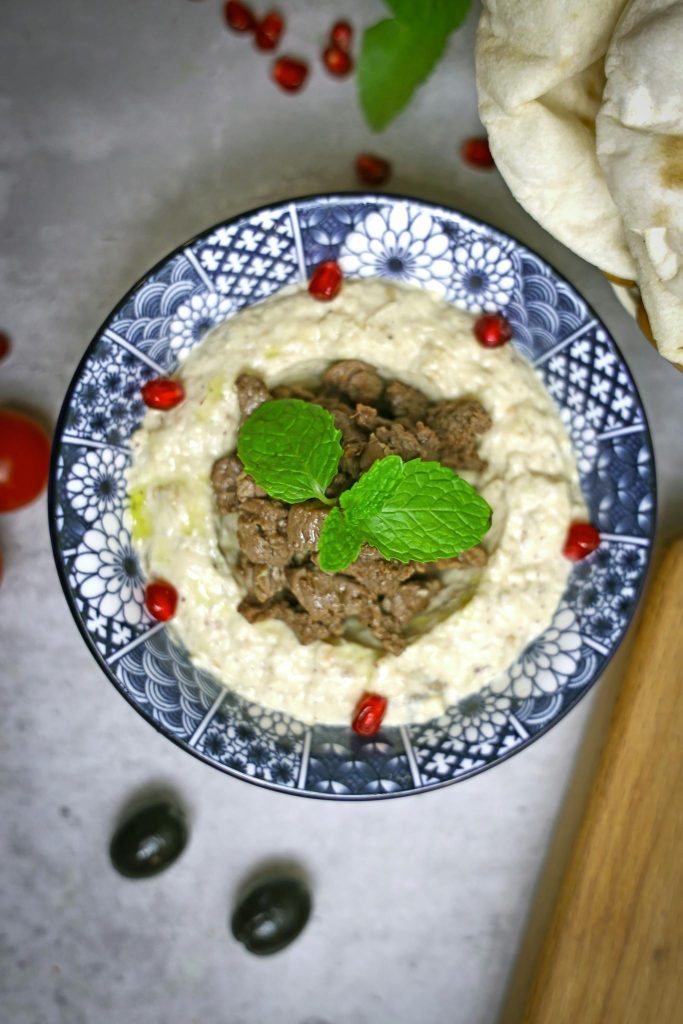 A bowl of hummus with meat and mint