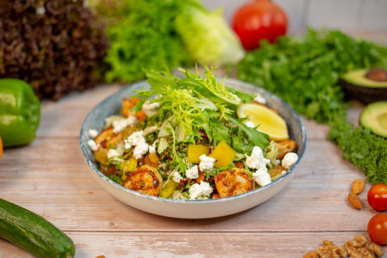 A bowl of salad with vegetables and nuts on a wooden table