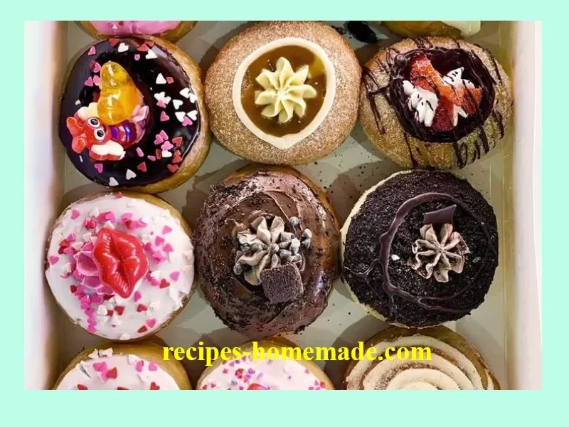 Assorted donuts including glazed, chocolate, and sprinkles on a wooden table.