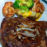 Boneless steak with onions and shrimp served on a baked potato