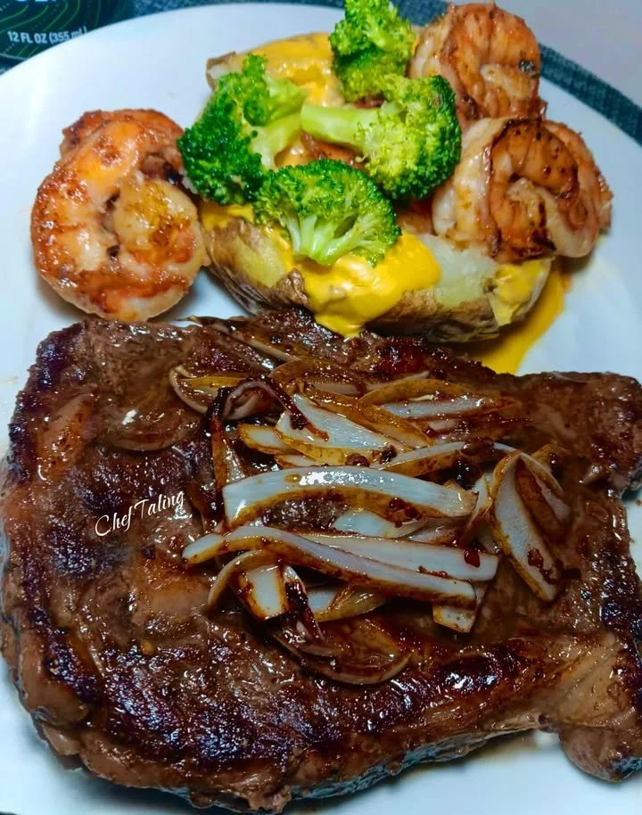 Boneless steak with onions and shrimp served on a baked potato