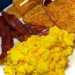 A plate of breakfast for dinner with eggs, pancakes, and bacon.