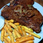 Garlic butter steak with grilled onions and parmesan fries served on a plate.