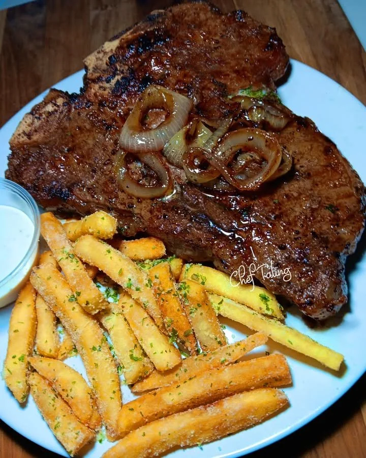 Garlic butter steak with grilled onions and parmesan fries served on a plate.