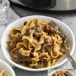 Slow cooker beef and noodles dish ready to serve with herbs and spices.